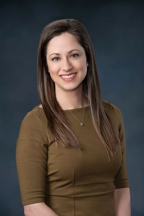 Portrait of Dr. Audrey Dean – dermatologist Professional portrait of Dr. Audrey Dean, dermatologist at Millcreek Dermatology, smiling warmly in a brown dress against a dark studio background – Dr Dean dermatologist